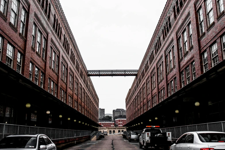 a couple of cars driving down a street next to tall buildings, inspired by Thomas Struth, pexels contest winner, [[empty warehouse]] background, steel archways, brown, cleveland