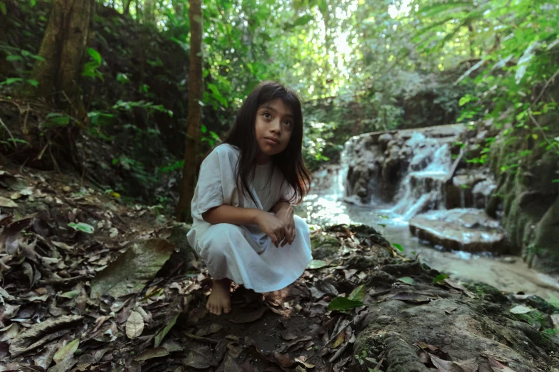 a young girl crouches in front of a waterfall, an album cover, by david rubín, sumatraism, 8 k film still, thumbnail, indigenous, multiple stories