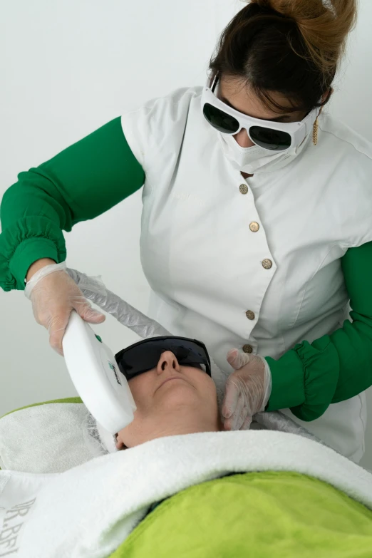 a woman getting a laser treatment in a beauty salon, a photo, inspired by Eva Švankmajerová, wearing facemask and sunglasses, with a white background, a green, white neck visible