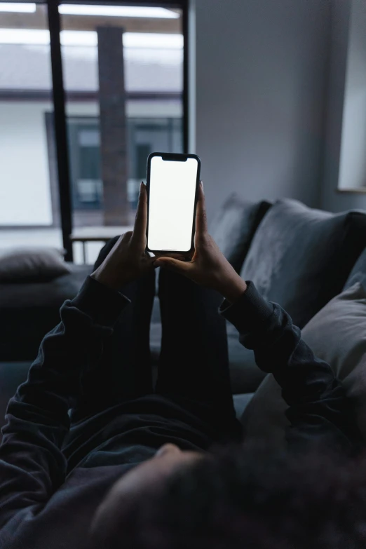 a person laying on a couch using a cell phone, by James Morris, trending on pexels, standing in corner of room, screen light, on a gray background, no lights in bedroom