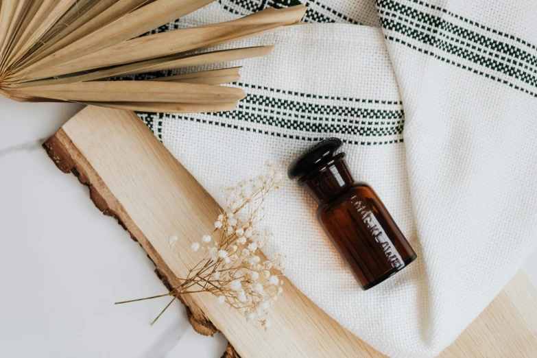 a bottle of essential oil sitting on a towel next to a fan, inspired by Ceferí Olivé, unsplash, arts and crafts movement, gypsophila, brown, background image, glass jar