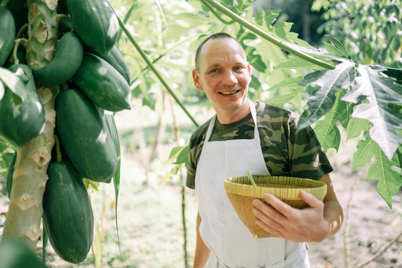 a man in an apron holding a basket of fruit, a photo, inspired by Jan Konůpek, pexels contest winner, wearing a melon, avatar image, farming, slightly smiling