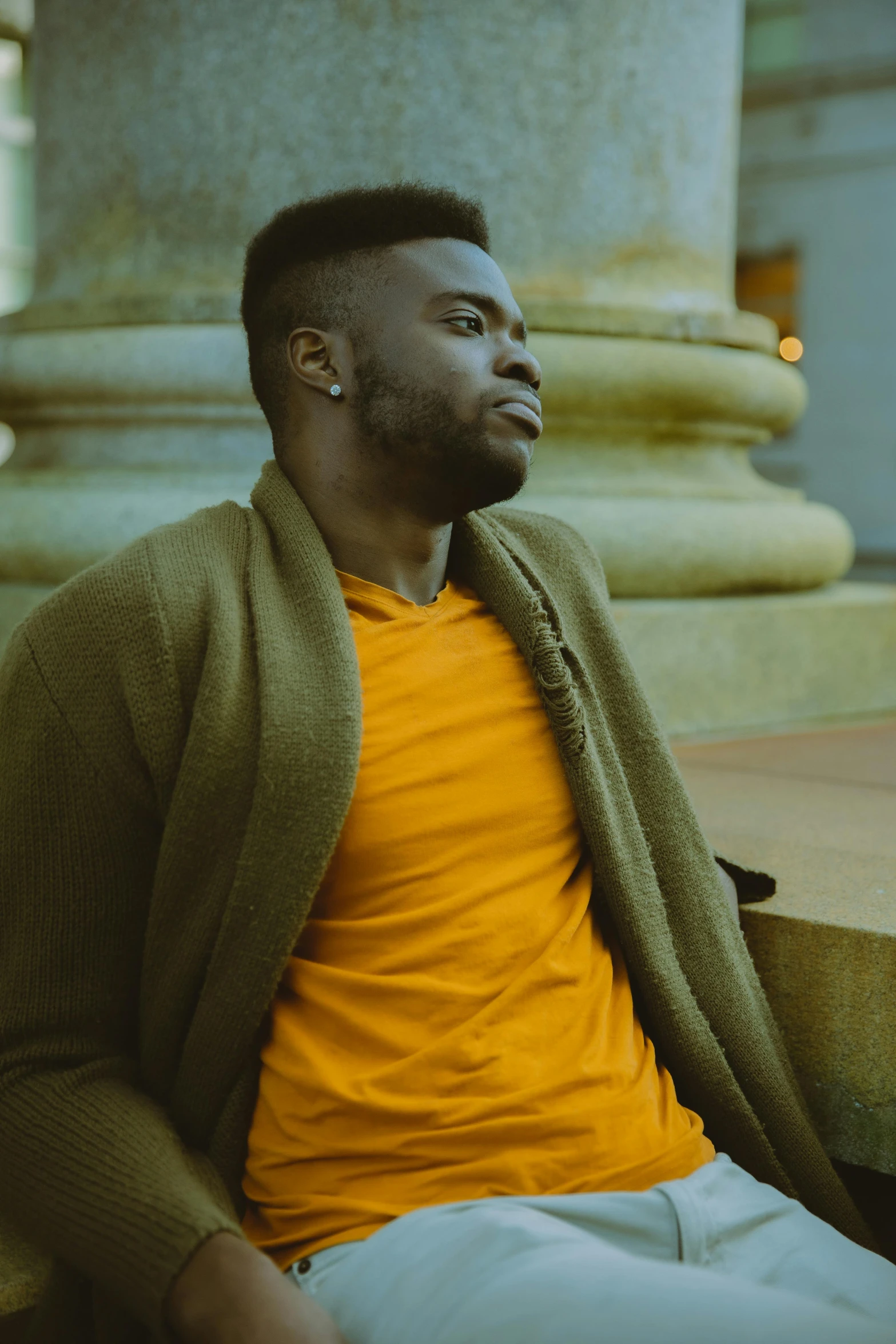 a man sitting on the steps of a building, an album cover, inspired by Paul Georges, pexels contest winner, he is wearing a brown sweater, jaylen brown, yellow hue, looking to his side