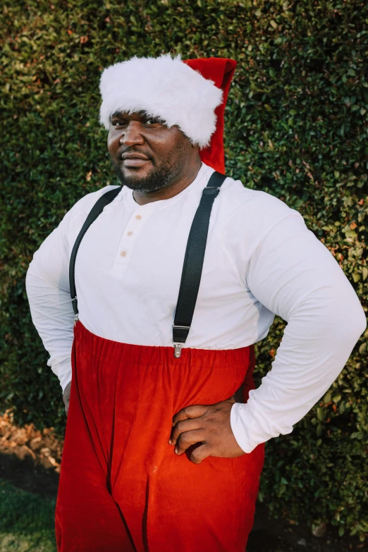 a man in a santa hat standing in front of a hedge, an album cover, featured on reddit, happening, shaq, white skirt and barechest, wearing plumber uniform, profile image