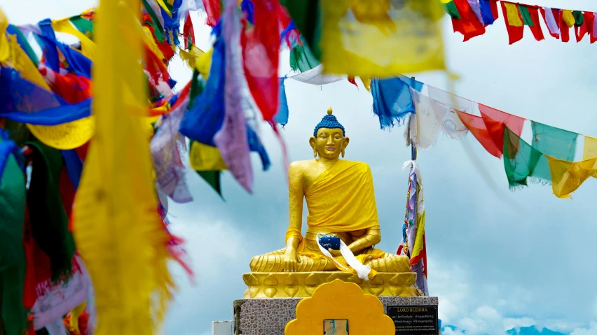 a golden buddha statue surrounded by colorful flags, a statue, unsplash, blue and yellow theme, nepal, 🦩🪐🐞👩🏻🦳, avatar image