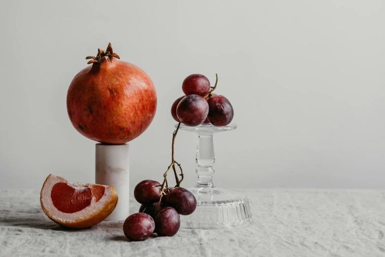 a bunch of grapes and a pomegranate on a table, trending on pexels, visual art, white marble interior photograph, background image, glassware, on a pedestal