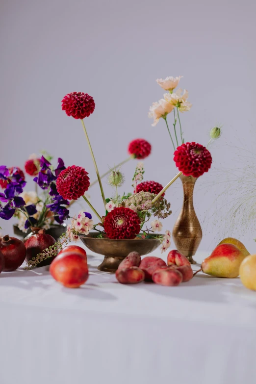 a white table topped with fruit and flowers, by Jessie Algie, shutterstock contest winner, vanitas, red gold color palette, product shoot, dahlias, sleek flowing shapes