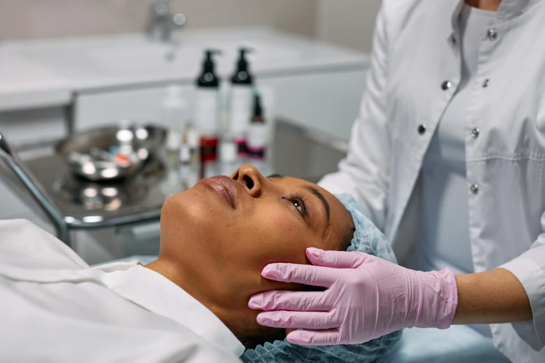 a woman getting a facial massage at a beauty salon, by Meredith Dillman, trending on pexels, renaissance, with a lab coat, dark skinned, cysts, on an operating table