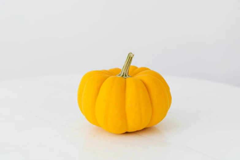 a small yellow pumpkin sitting on top of a white table, by Nicolette Macnamara, product photograph, hero prop, round-cropped, full colour