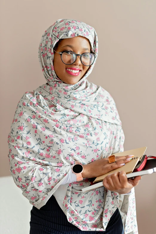 a woman in a hijab holding a book, floral patterned skin, wearing eyeglasses, looking confident, standing in class