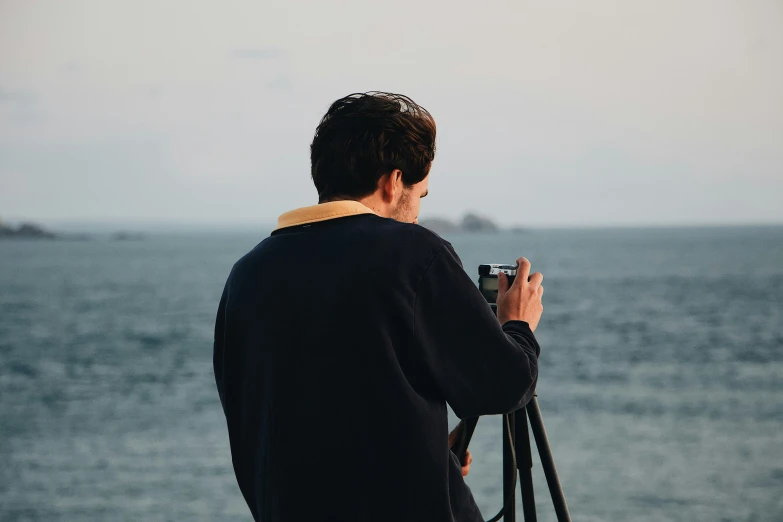 a man taking a picture of the ocean with a camera, a picture, head and shoulders 8 0 mm camera, facing away from camera, coloured photo, portrait photo