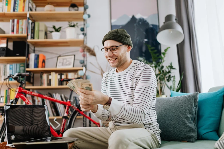 a man sitting on a couch reading a book, pexels contest winner, flaunting his wealth, sitting at a computer, aboriginal australian hipster, cash on a sidetable