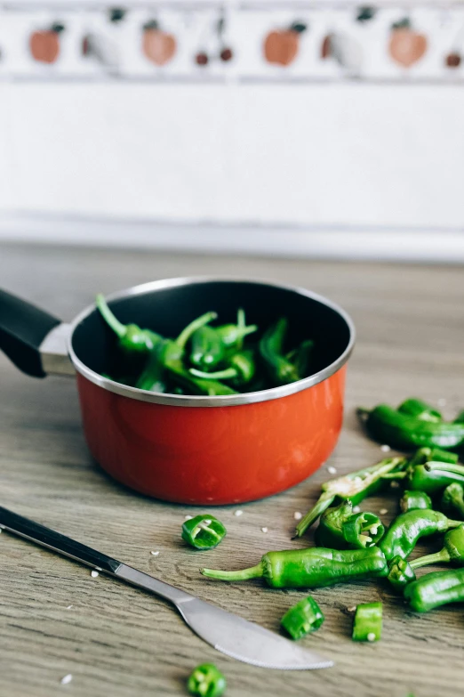 a pan filled with green peppers next to a knife, by Julia Pishtar, unsplash, holding hot sauce, ceramic pot, multiple stories, red