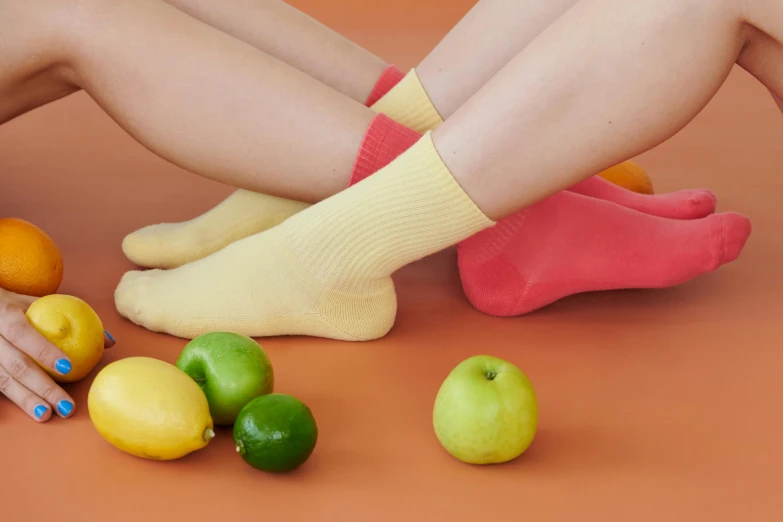 a woman sitting on the ground next to a pile of fruit, inspired by Sarah Lucas, dribble, socks, light yellow, skincare, close up shot from the side