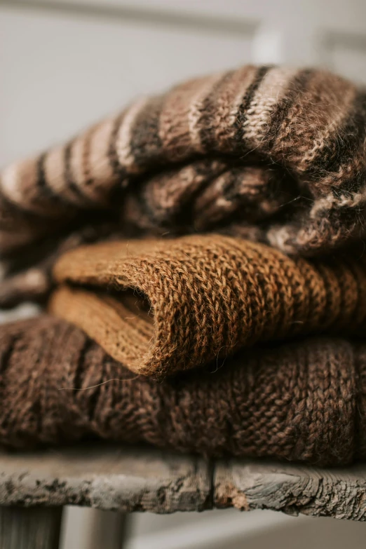 a pile of sweaters sitting on top of a wooden table, by Adam Marczyński, trending on unsplash, tan and brown fur, chocolate. rugged, organic detail, a pair of ribbed