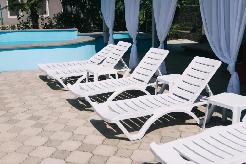 a row of lawn chairs next to a swimming pool, white finish, bizzaro, oasis, no shade