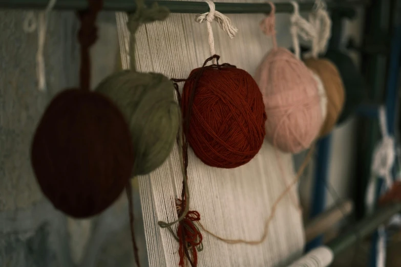 a bunch of balls of yarn hanging on a wall, an album cover, inspired by Toss Woollaston, pexels contest winner, olive green and venetian red, in a workshop, natural muted tones, close-up shot taken from behind