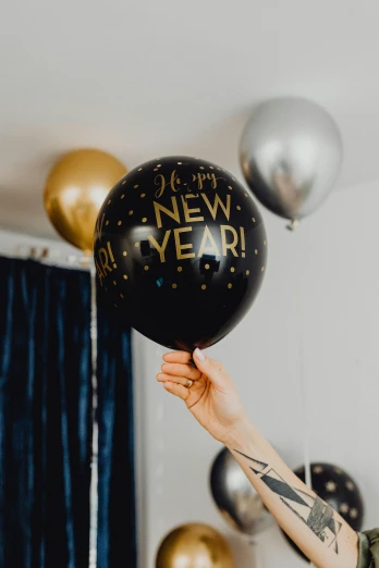 a woman holding a black and gold new year balloon, by Julia Pishtar, trending on pexels, low detail, decoration around the room, hey, blue silver and black