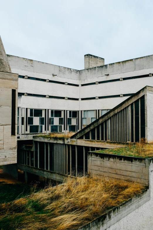 a building sitting on top of a grass covered field, unsplash, brutalism, war theatre, concrete balcony, 1990s photograph, old library