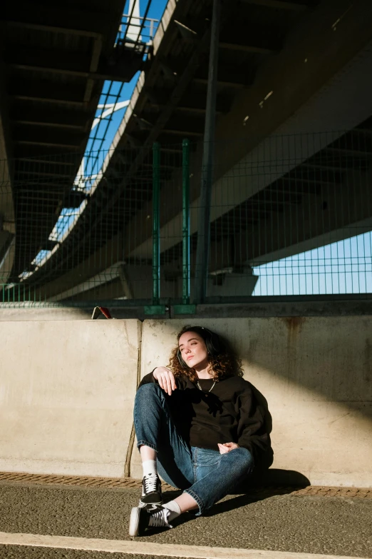 a woman sitting on the ground in front of a bridge, unsplash, renaissance, androgynous person, backlit portrait, “gas station photography, curly haired