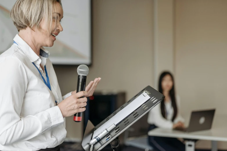 a woman in a white shirt is speaking into a microphone, a cartoon, unsplash, academic art, whiteboards, mid shot photo, 15081959 21121991 01012000 4k, thumbnail