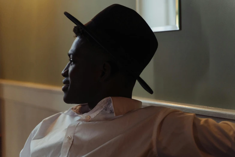 a man sitting on a couch wearing a hat, by Richmond Barthé, pexels contest winner, les nabis, side profile view, dark skinned, soft light from the side, alphonse fly