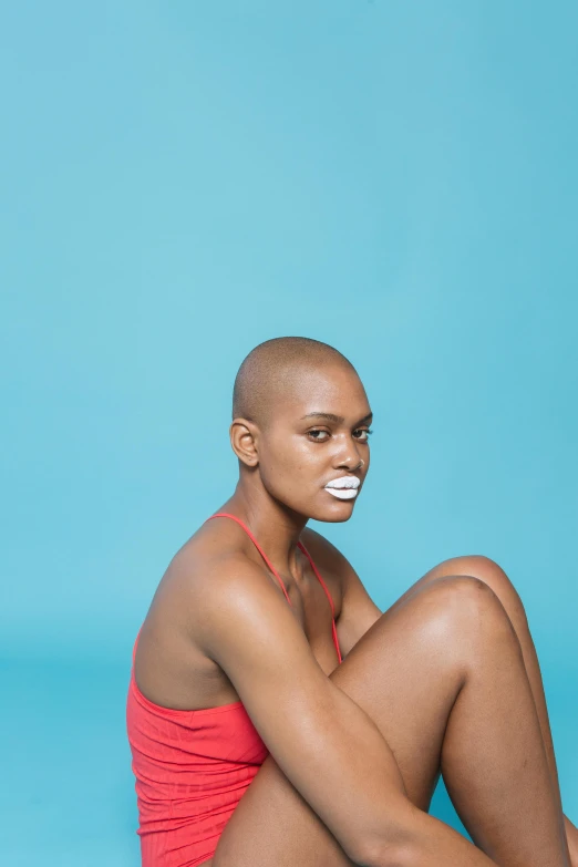 a woman sitting on the ground with her legs crossed, inspired by Barkley Hendricks, pexels contest winner, dada, shaved sides, relaxed. blue background, bite her lip, sunburn