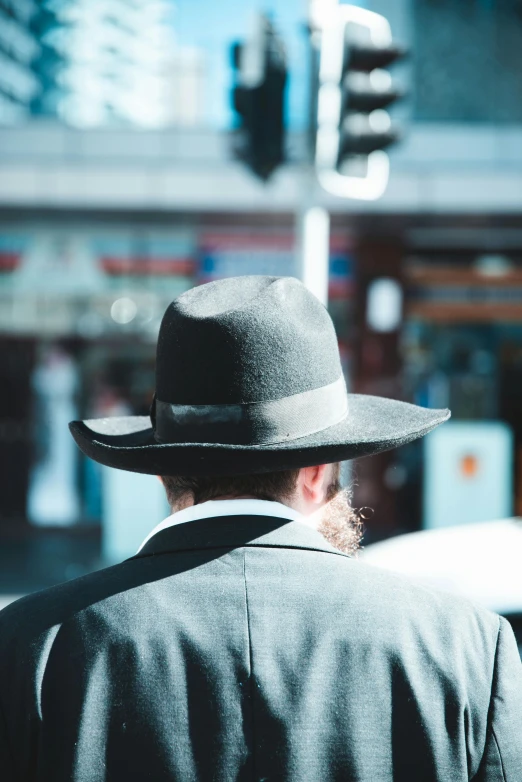 a man in a hat is walking down the street, unsplash, symbolism, hebrew, looking from behind, subject detail: wearing a suit, australian