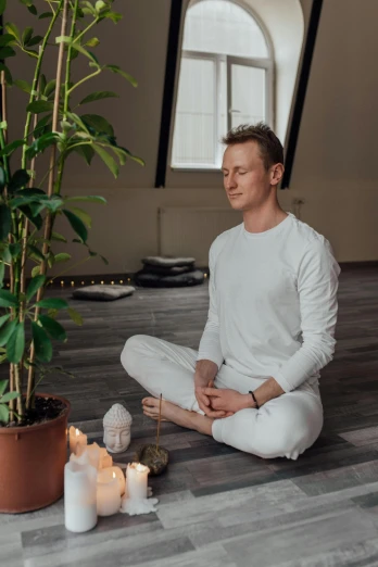 a man sitting on the floor next to a potted plant, a picture, by Adam Marczyński, meditating in lotus position, profile image, low quality photo, markus gunnar