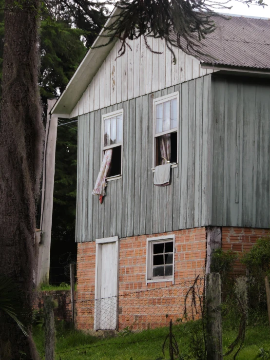 a house sitting in the middle of a lush green field, an album cover, unsplash, old lumber mill remains, freddy mamani silvestre facade, window, pareidolia