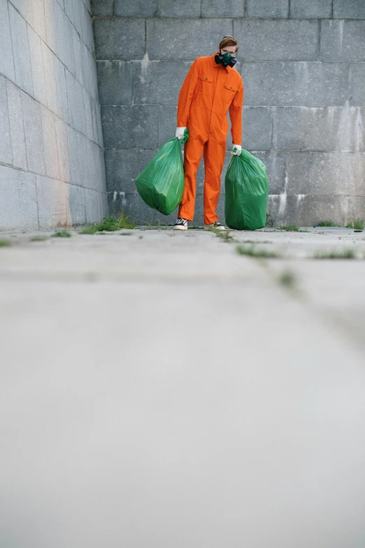 a man in an orange jumpsuit holding two green bags, shutterstock, conceptual art, trash ; basement, sweeping, instagram picture, prison jumpsuit