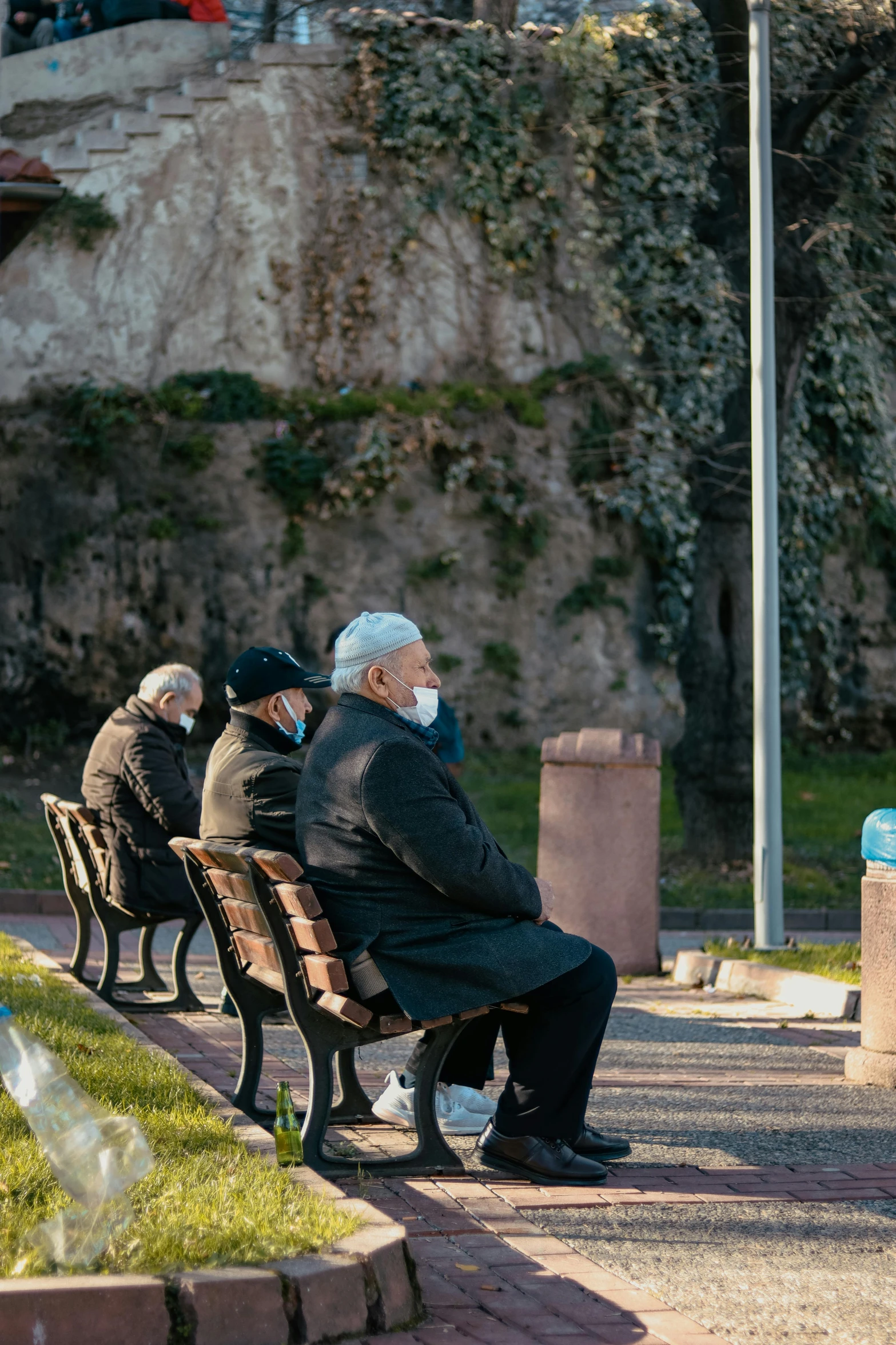 a group of people sitting on top of a wooden bench, a statue, old man doing with mask, sitting alone, healthcare, overlooking