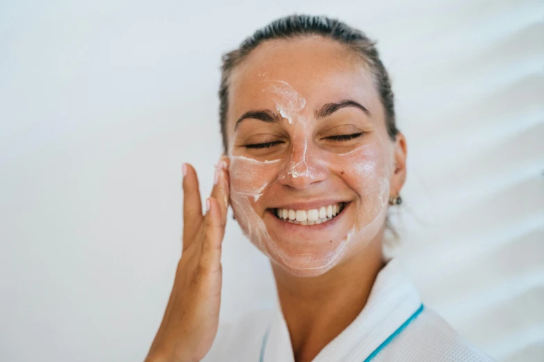 a woman smiles as she puts a facial mask on her face, pexels contest winner, frosting on head and shoulders, manuka, profile image, coerent face and body