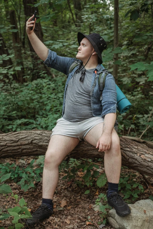 a man sitting on a log taking a picture of himself, by Ryan Pancoast, genderless, thick thighs, on a branch, dressed as a scavenger