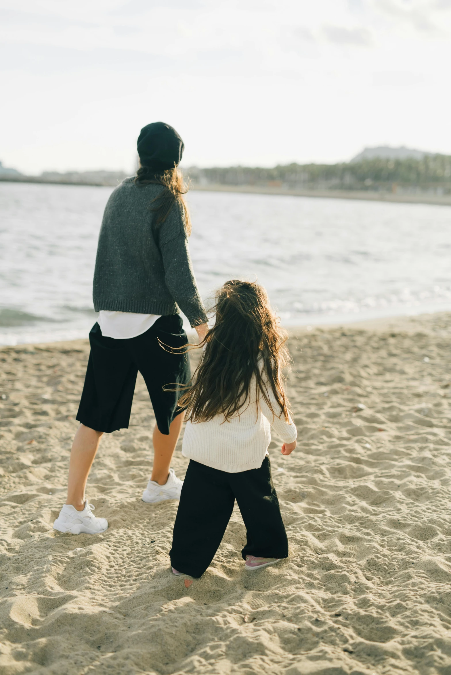 a man and a little girl walking on a beach, by Lucia Peka, trending on unsplash, incoherents, black haired girl wearing hoodie, wearing black shorts, lesbians, laying on sand