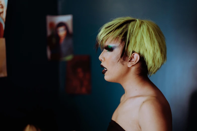 a woman with green hair standing in front of a mirror, inspired by Nan Goldin, unsplash, yellow and black, drag, diverse haircuts, looking to his left