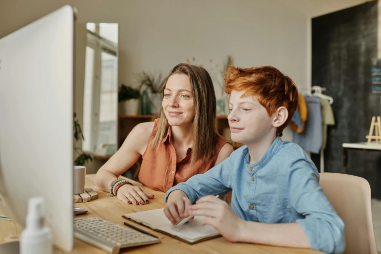 a couple of people sitting at a table in front of a computer, brunette boy and redhead boy, school curriculum expert, lachlan bailey, parents watching