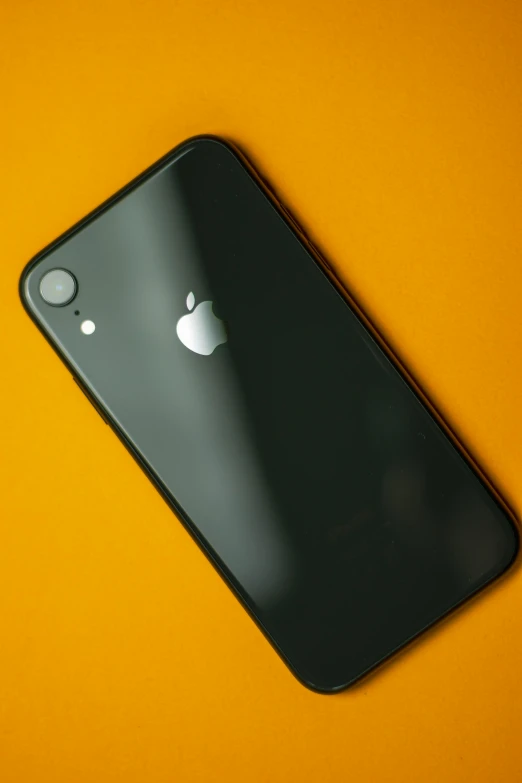 an iphone sitting on top of a yellow surface, pexels, black on black, apple orange, 2049, back