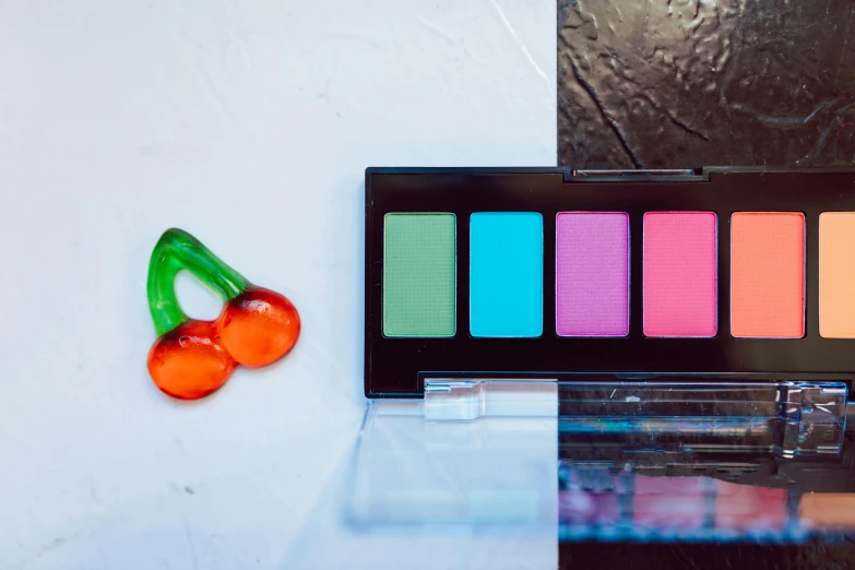 a close up of a palette of eyeshadow next to a cherry, a pop art painting, inspired by Elsa Bleda, unsplash, bauhaus, pastel neon, rectangle, green and pink, high contrast plastic