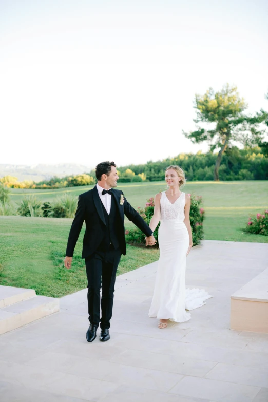 a man in a tuxedo and a woman in a wedding dress holding hands, walkway, gregoire and manon, golf course, greek setting