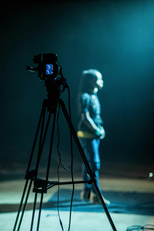 a man standing in front of a camera on a tripod, a hologram, by David Begbie, unsplash, video art, theatre equipment, girl in studio, camera looking down upon, on a stage