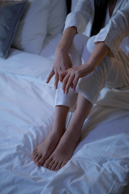 a woman sitting on top of a bed covered in white sheets, feet and hands, poorly lit, walking down, sitting with wrists together