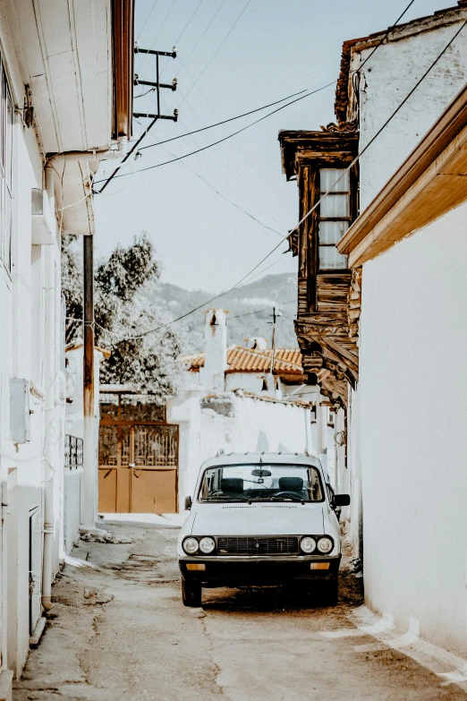 a car parked on the side of a narrow street, pexels contest winner, renaissance, white and gold color palette, behind a tiny village, 70s photo, byzantine