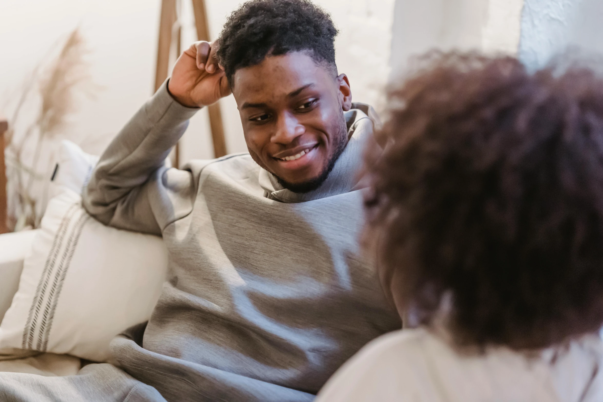 a man sitting on top of a couch next to a woman, pexels contest winner, brown skin man with a giant grin, reaching out to each other, black teenage boy, wearing a grey robe