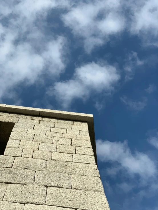 a clock that is on the side of a building, an album cover, unsplash, brutalism, blue sky with a few clouds, stone bricks, low quality photo, head looking up