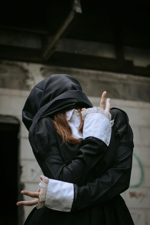 a woman standing in front of a brick building, a statue, unsplash, romanticism, vampire nun, hugging each other, black hoodie, mime