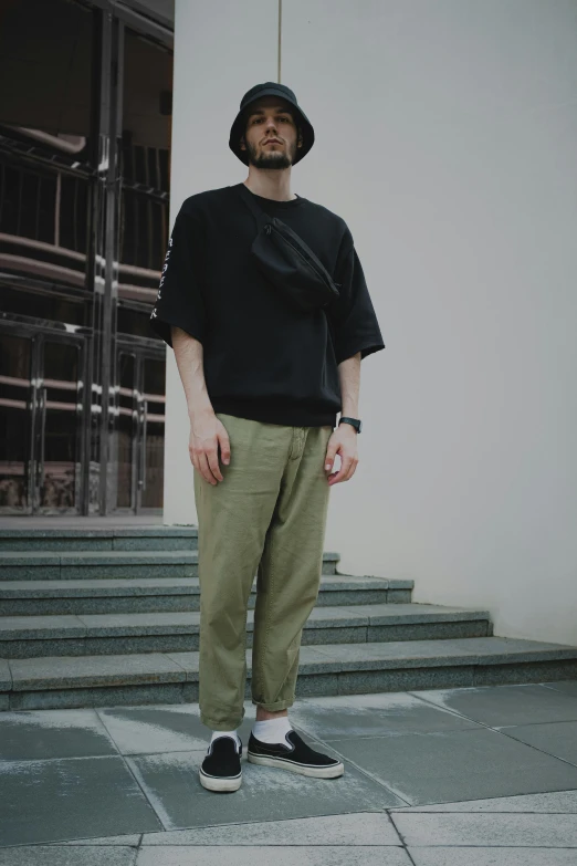 a man standing on the steps of a building, a picture, unsplash, shin hanga, acronym p31-ds pants, olive green, wearing a black!! t - shirt, color photograph