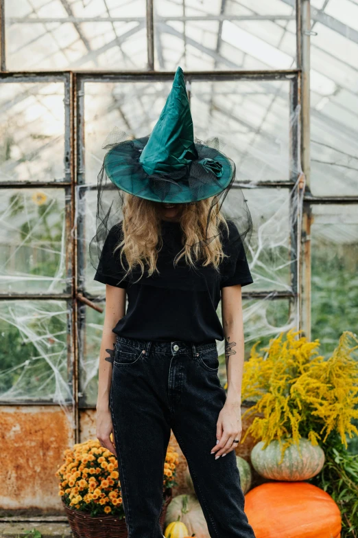 a woman wearing a witch hat standing in front of a greenhouse, trending on pexels, green corduroy pants, black and teal paper, costume, indoor picture