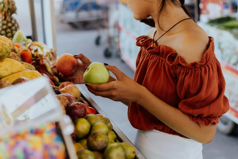 a woman standing in front of a fruit stand, trending on pexels, one holds apple in hand, profile image, sitting on a store shelf, wearing a cropped top