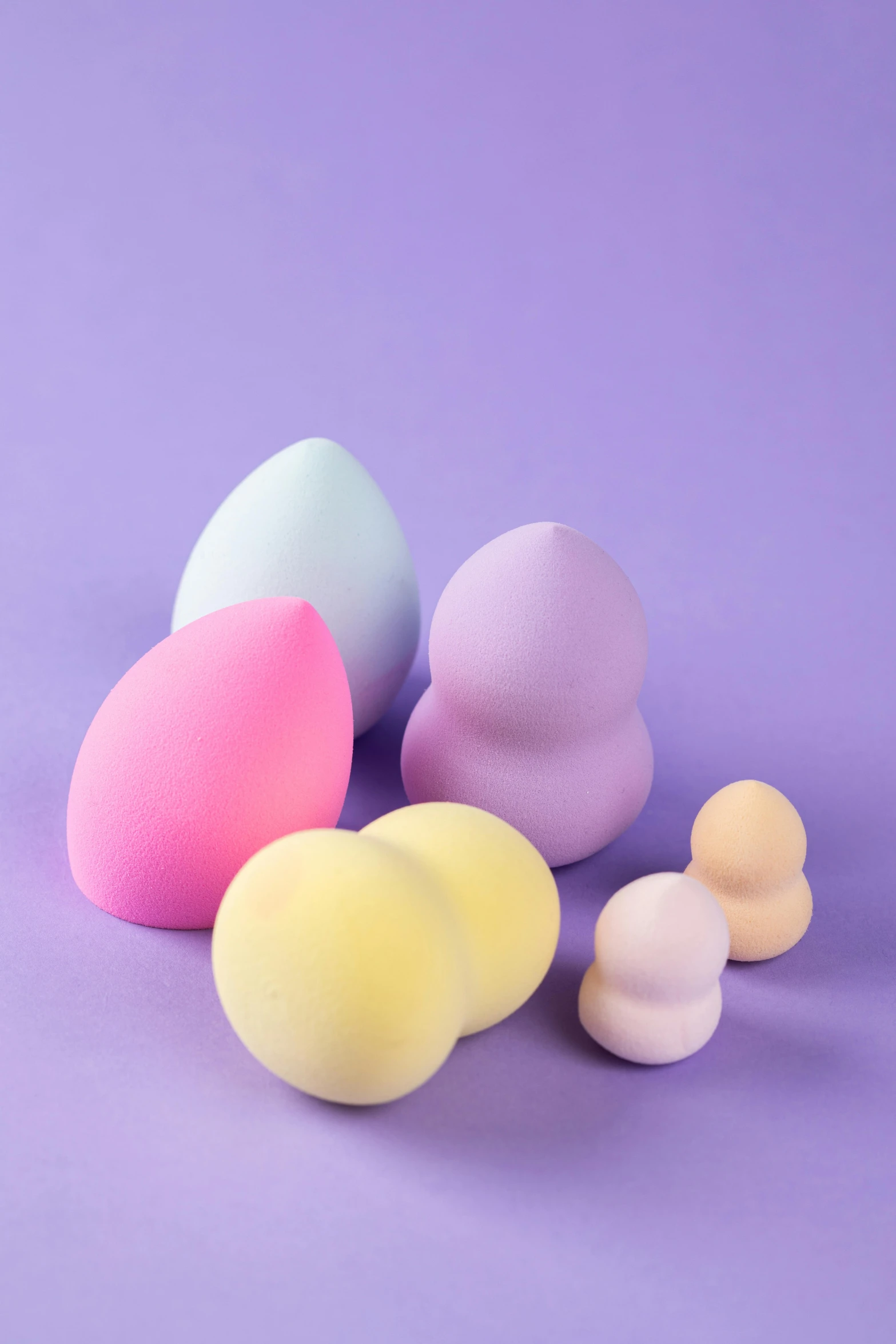 a group of makeup sponges on a purple background, by Doug Ohlson, soft curvy shape, various sizes, pastel', figurines